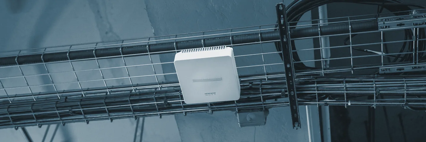 A wireless access point mounted on a wire cable tray under an industrial ceiling.