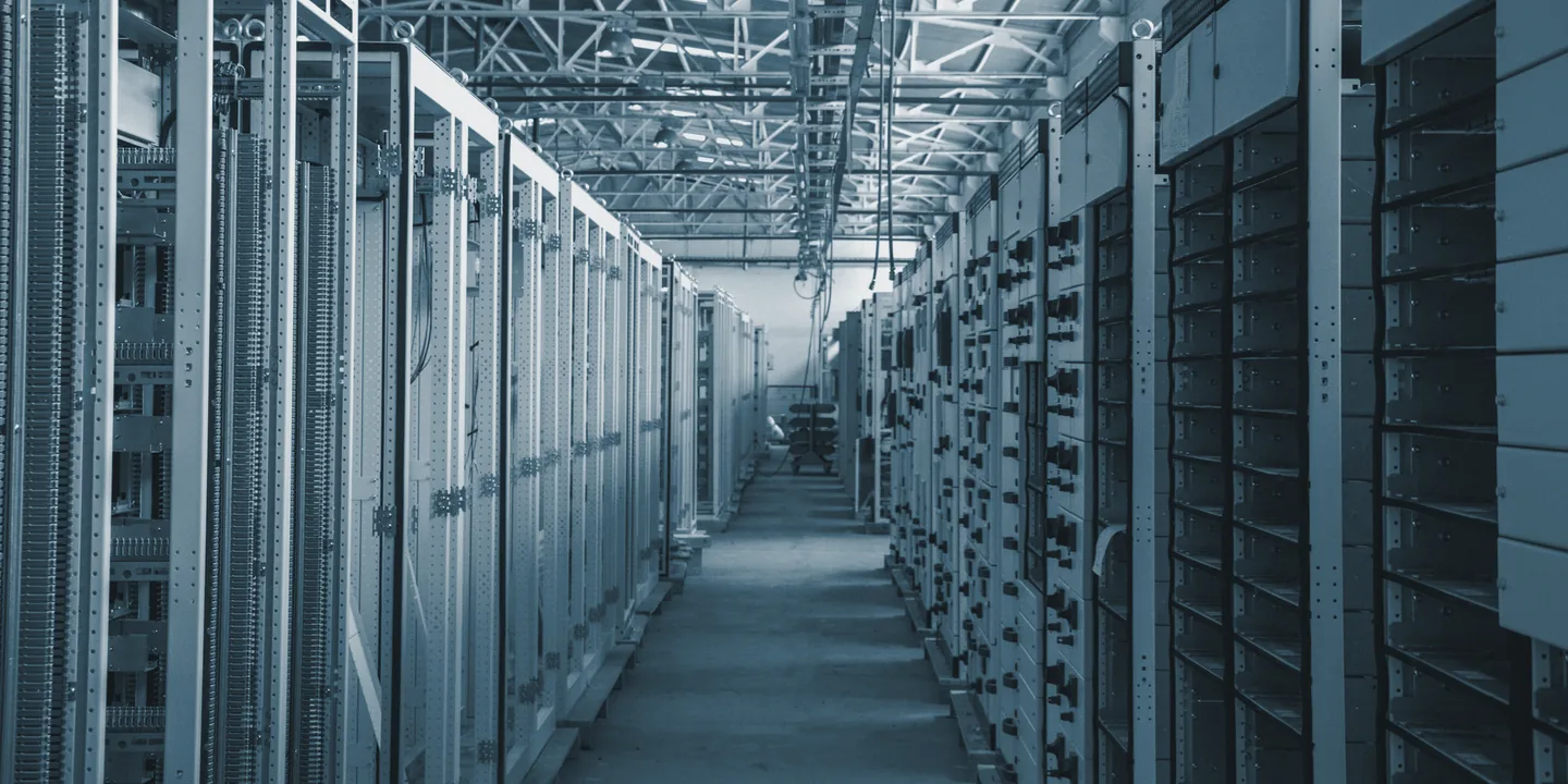 A long aisle between two rows of open equipment cabinets in a daylit industrial hall.